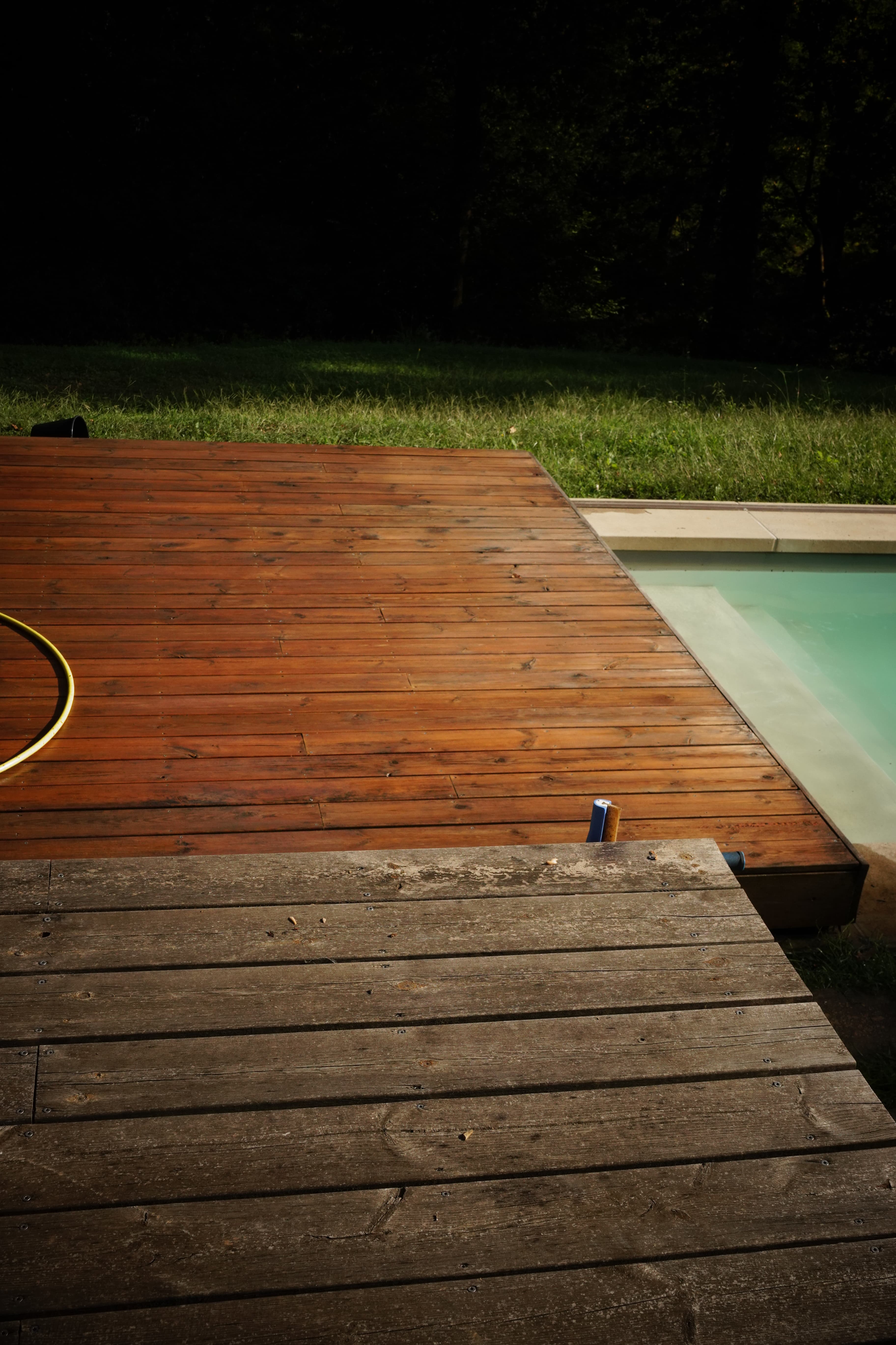 Terrasse en bois avec contraste entre planches vieillies et lasurées à côté d'une piscine.
