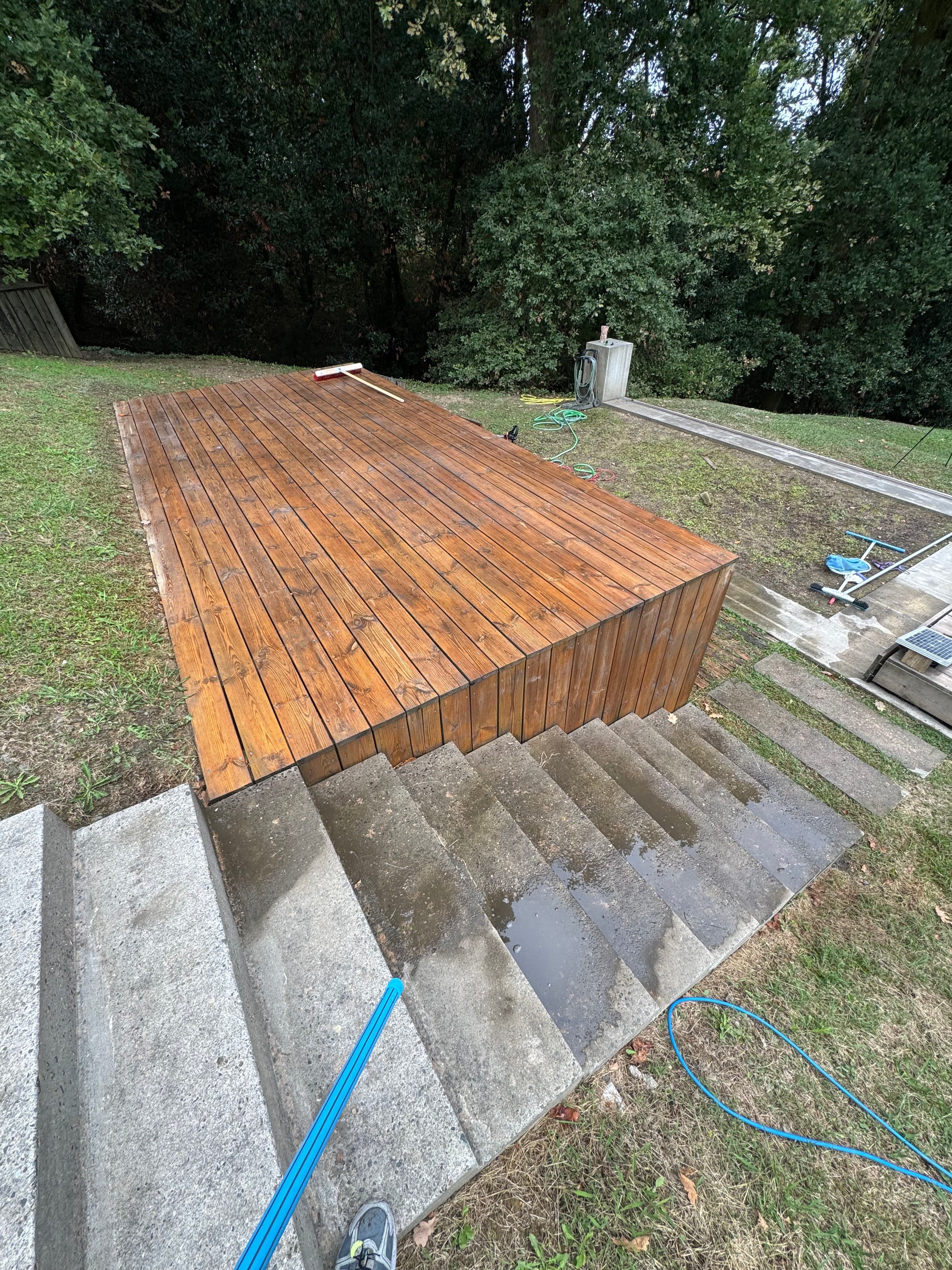 Terrasse en bois brun brillant à côté de marches en béton mouillées dans un jardin.
