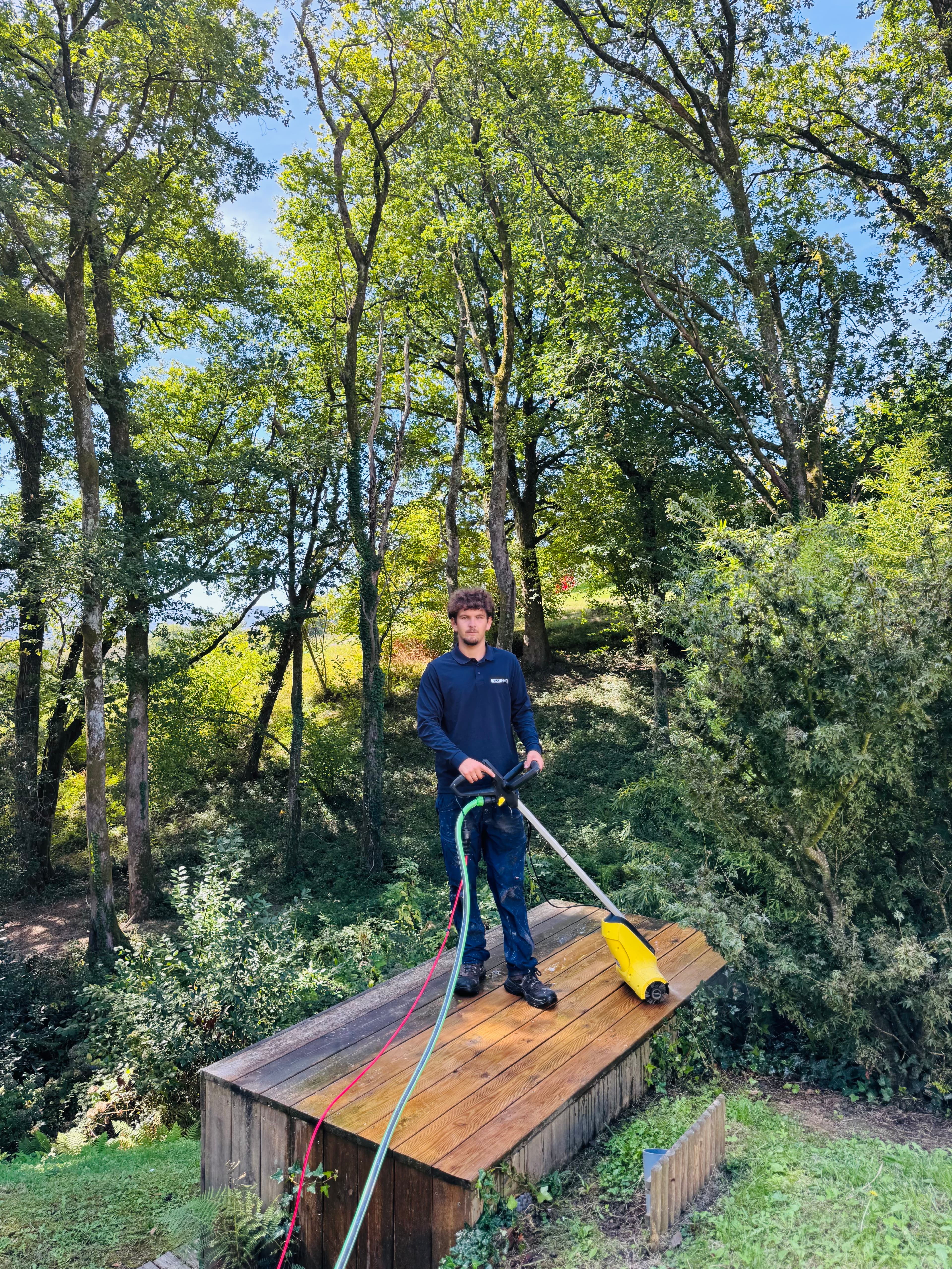 Homme nettoyant une terrasse en bois avec un nettoyeur haute pression en pleine forêt.