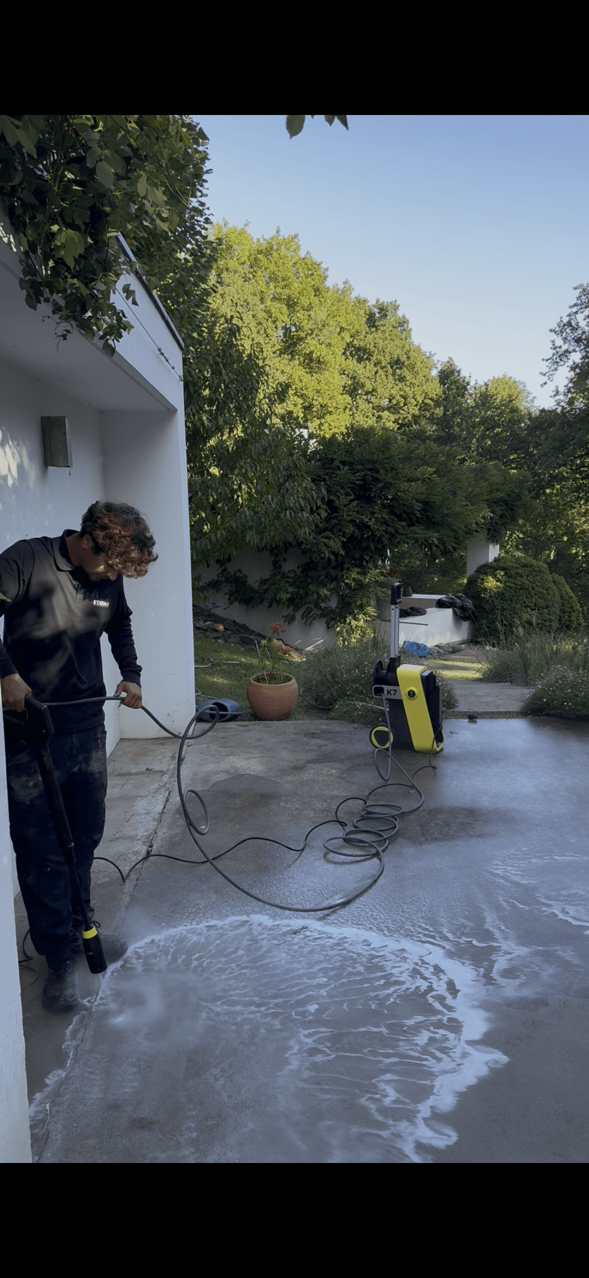 Un homme nettoie une terrasse avec un nettoyeur haute pression dans un jardin verdoyant.