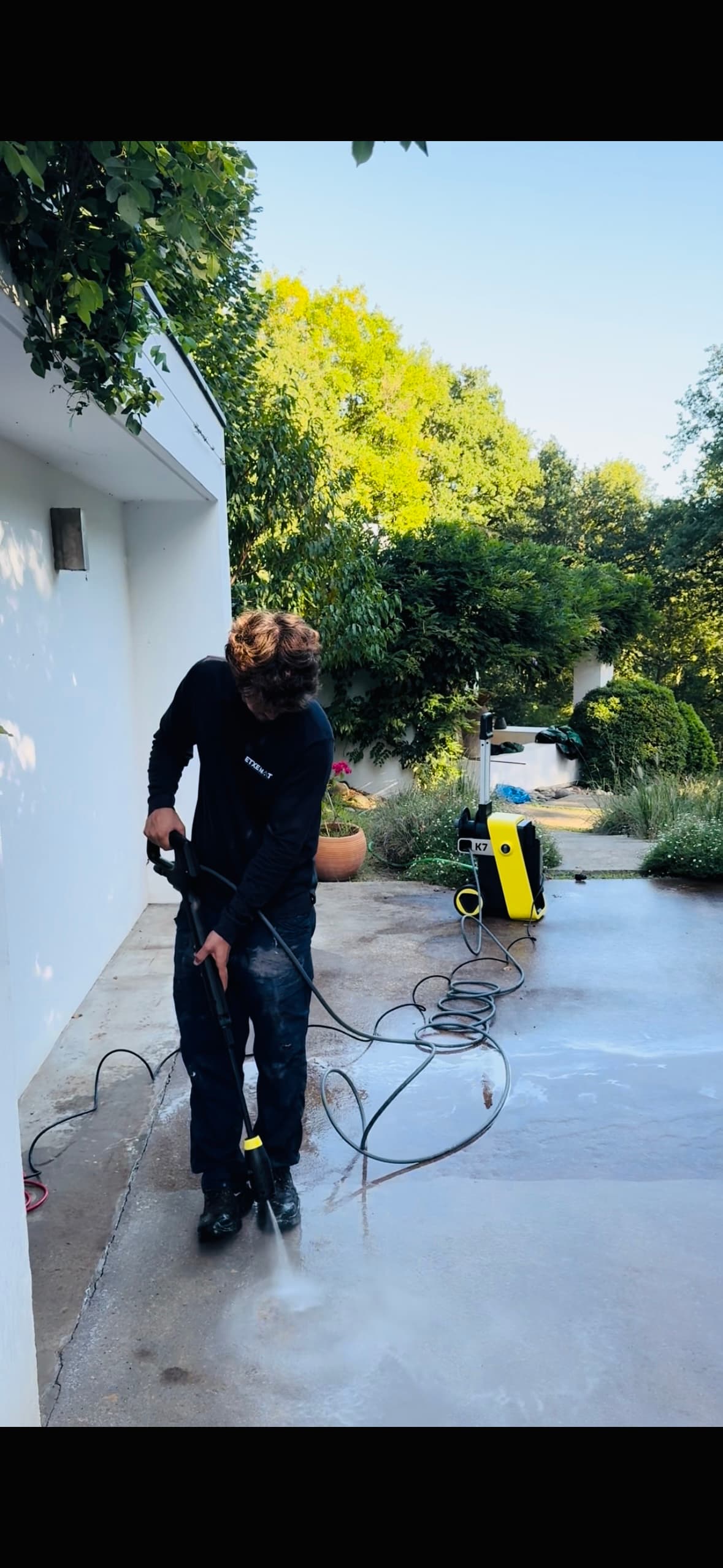 Un homme utilise un nettoyeur haute pression jaune pour nettoyer une terrasse en béton.