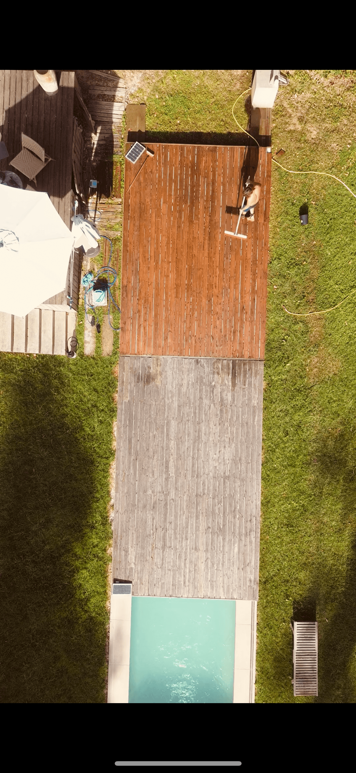Vue aérienne d'un homme traitant une terrasse en bois bicolore bordant une piscine.